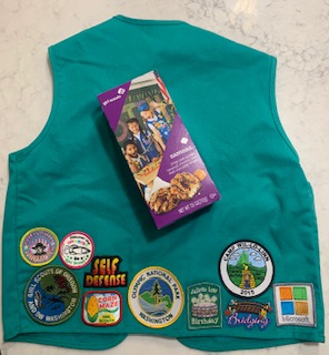 A retired Girl Scouts vest displays various badges in addition to the cookie sales badge. Girl Scout cookies cost $5 a box and the gluten free cookies cost $6. 