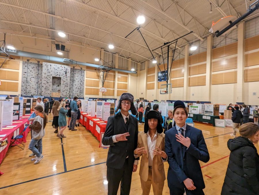 Soren Tucker, Anthony Herrera, and Henri Villeneuve stand amidst a busy exhibit hall. They are excited about their project.