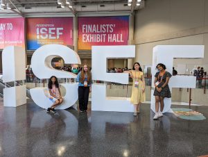 WLWV ISEF girls pose by the ISEF sign in the convention center, right in front of the finalist exhibit hall, where thousands of posters are set up for each project at the fair!