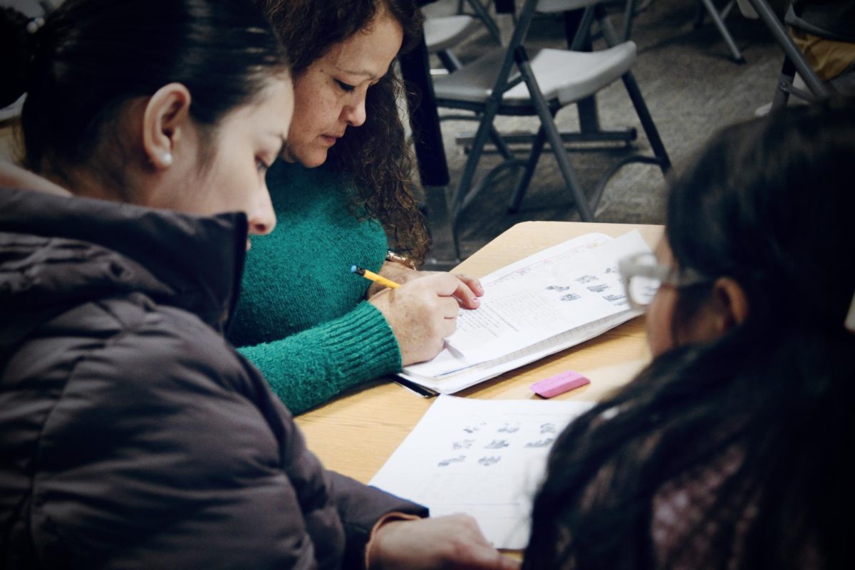Community members join Monday nights Family Empowerment Program session. A family practices newly-learned English grammar skills in practice books and converses fluently with the instructor.