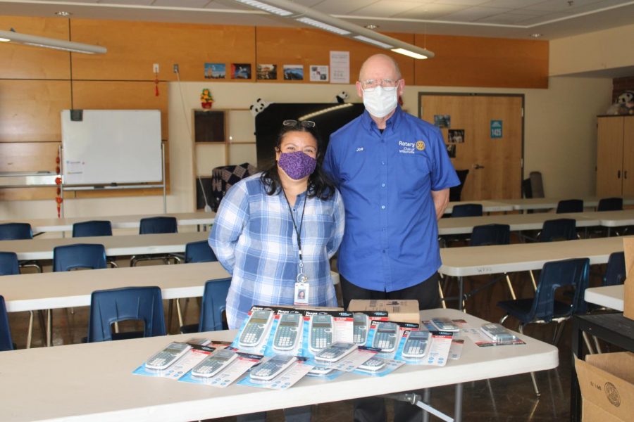 Joe from the Rotary Club of Wilsonville and Maria de Lourdes Horton of the Family Empowerment Center smile underneath their masks as they stand behind a table ladden with new calculators for the school.