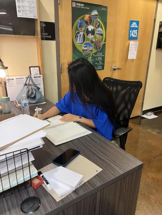 Ms. Zhang writing at her desk. She is excited to begin teaching at Wilsonville.