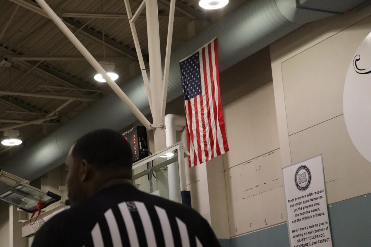 A cinematic shot of the American Flag inside the Wilsonville Gym. In the right corner is a referee watching the game.