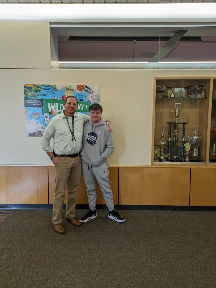 Atheltic Director Josh Davis and student Jonah Sandall having a good time. Behind them is an artwork titled "Wildcat Way," which illustrates the many successful clubs and organizations at Wilsonville High School. 