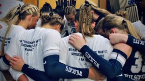 Wilsonville volleyball players huddle before a home match against Hood River. Pictured is Emily Holmes, Olivia Clark, Carli Vannoy, and Halle Harris, embracing their teammates as a final hoorah before breaking into the set. 