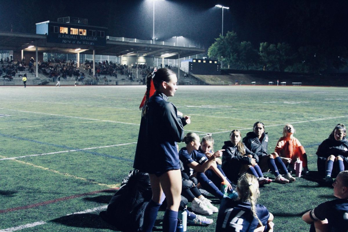 Senior player, Reese Holsey, speaks through encouragement and criticism towards her team during the half-time break of Wisonville Girls' soccer Varsity home match against West Linn. After facing the Lions and ending up 0:1 by the half time mark, the Cats lean in to their teammates and guiding coaches for the game plan. 