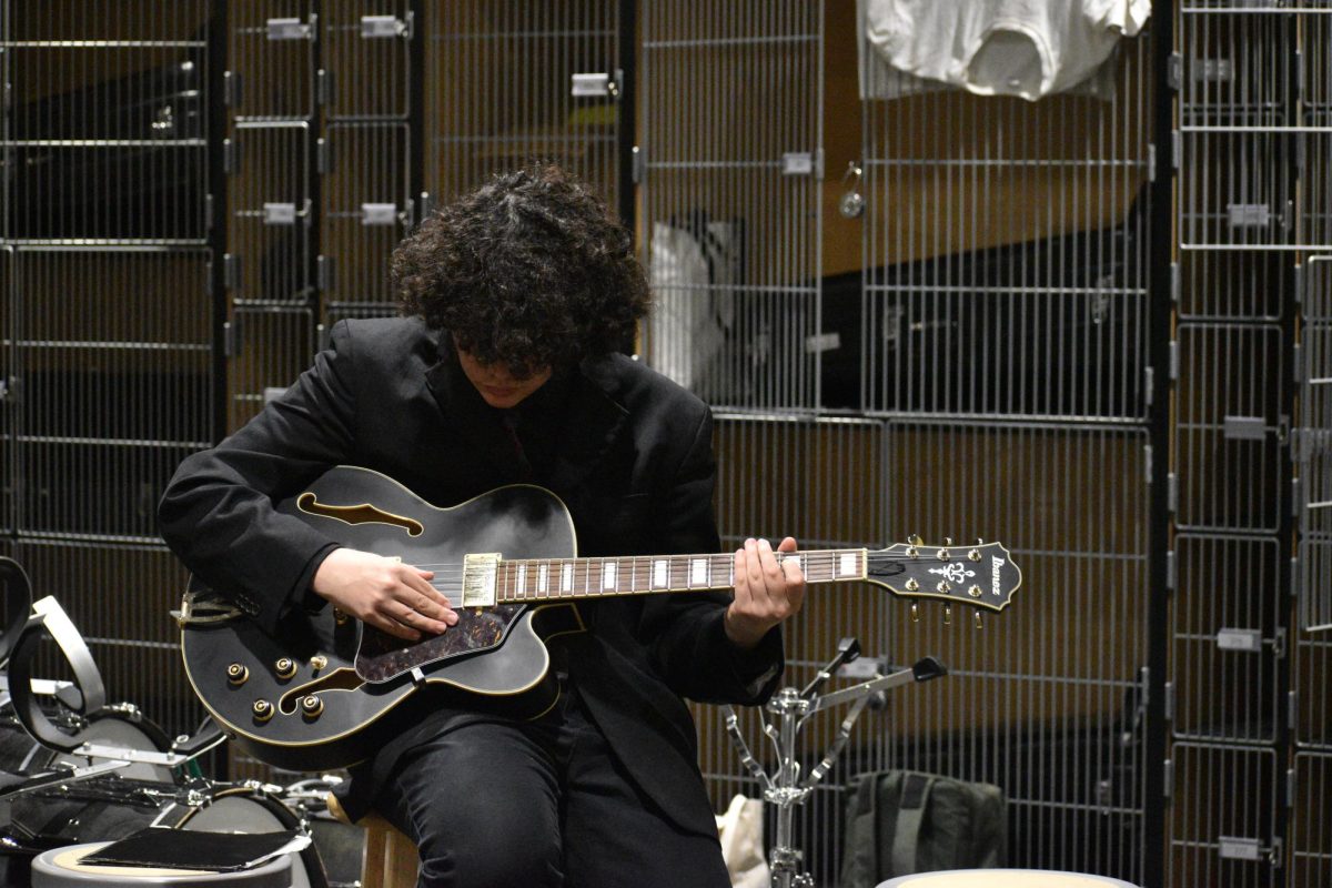 Zander Vigil strums his guitar minutes before the start of the concert. The "cages" behind are used to store instruments at the school when not in use. 