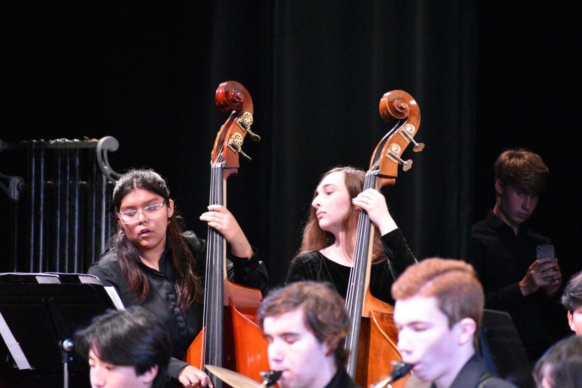 Sophia Culp and Kemberly Ramirez jam out in Jazz band. Behind them, Xander Layne records the performance, hidden in the shadows of the stage's legs. 