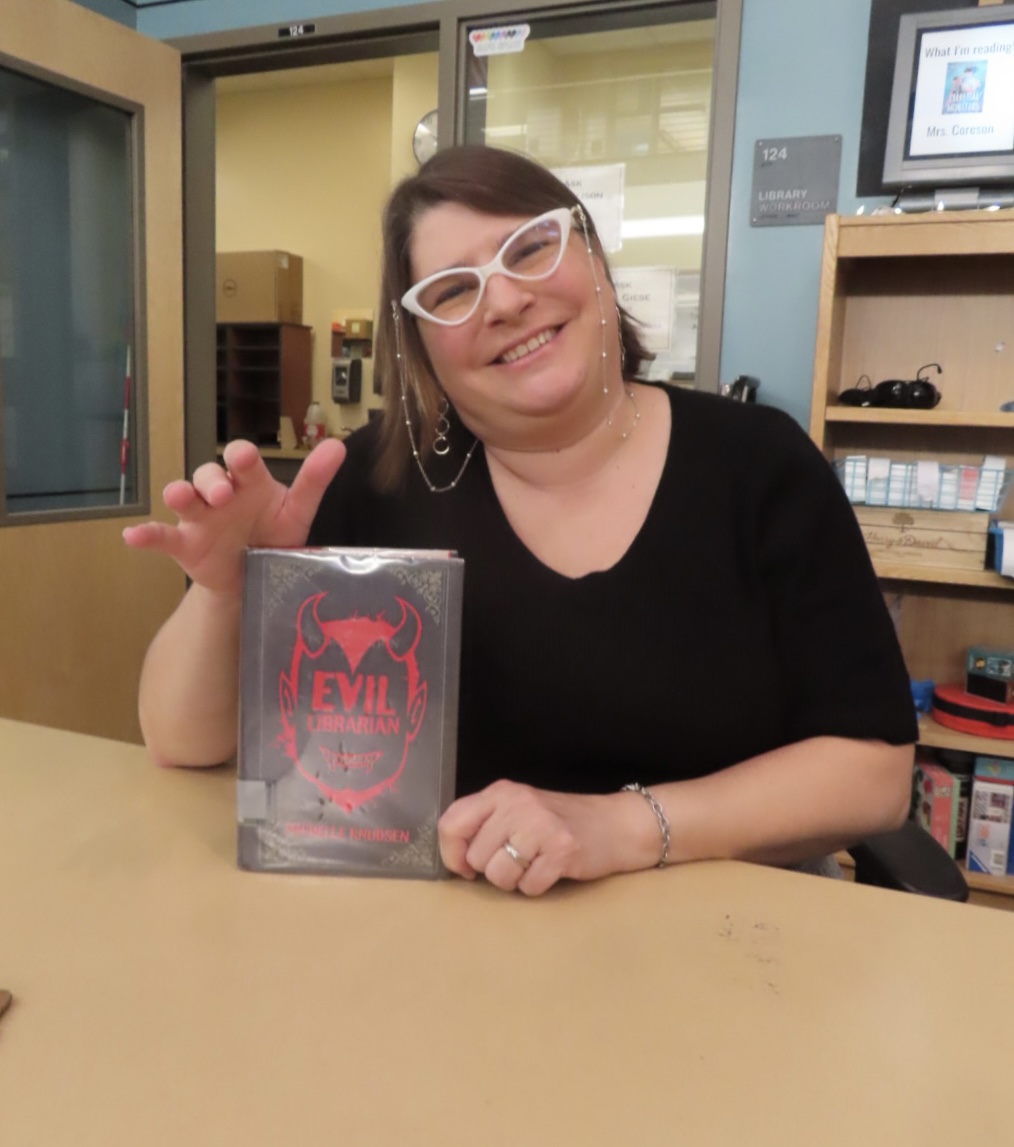 Mrs. Coreson, Wilsonville High School's librarian, holds up a popular book, one of many displayed around the library shelves. Friendly and welcoming, she's always ready to assist readers, and guide students towards stories. 