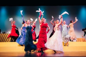 Women at the Neva Club come together for a energetic dance break, each person yielding a white handkerchief in her right hand. Lily (Sydney Cederberg), belts the song "Land of Yesterday," as she leads the group.