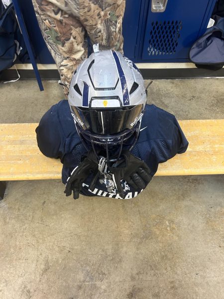 A players pads and helmet neatly organized in the locker room. A popular superstition is laying out all of your uniform before putting it on.