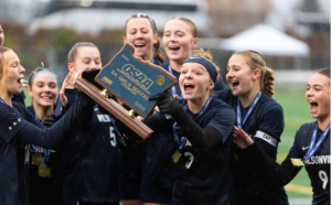 Wilsonville Girls Soccer players gather aroud the 5A State Championship plaque. They jump with joy after winning for the fourth year in a row.