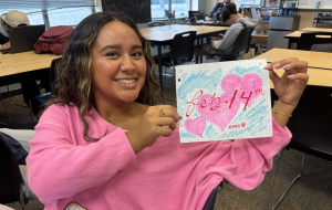 Milan de la Cruz holds up a Valentine's Day drawing showcasing traditional Valentine's Day artwork. Valentine's is marked by pink, hearts, xoxo, love, and other iconic staples!