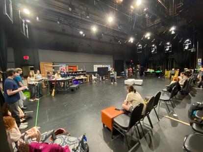 Students involved in the Once-In-a-Lifetime Play sit in the Black Box practicing for their performance. Seats are arranged for the audience around the play setting.
