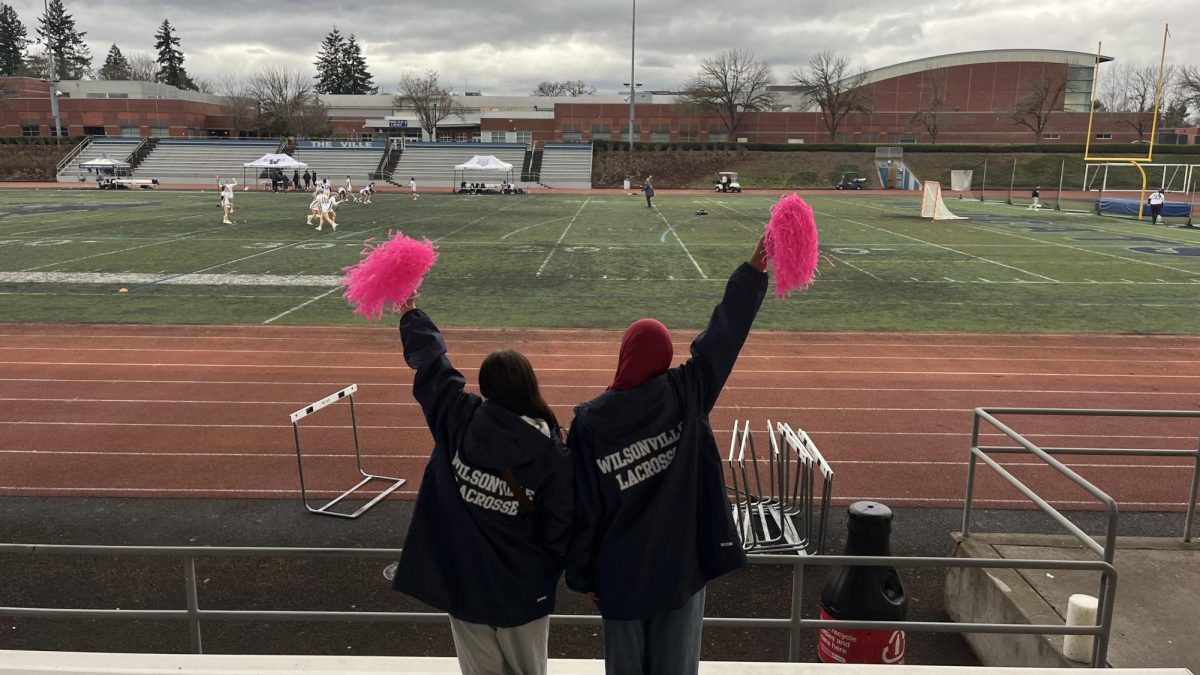 Wilsonville students Sophia Best and Mariam Moussa cheer for the Wilsonville Girls Lacrosse team during one of their games. Student attendance is low, but excitement is still high.