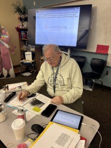 Substitute Teacher Mr. Russel works hard at his desk as he watches over the students in his class. He reads the sub plans that the previous teacher gave him.