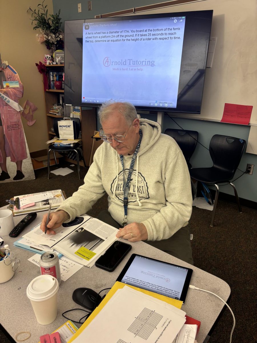Substitute Teacher Mr. Russel works hard at his desk as he watches over the students in his class. He reads the sub plans that the previous teacher gave him.