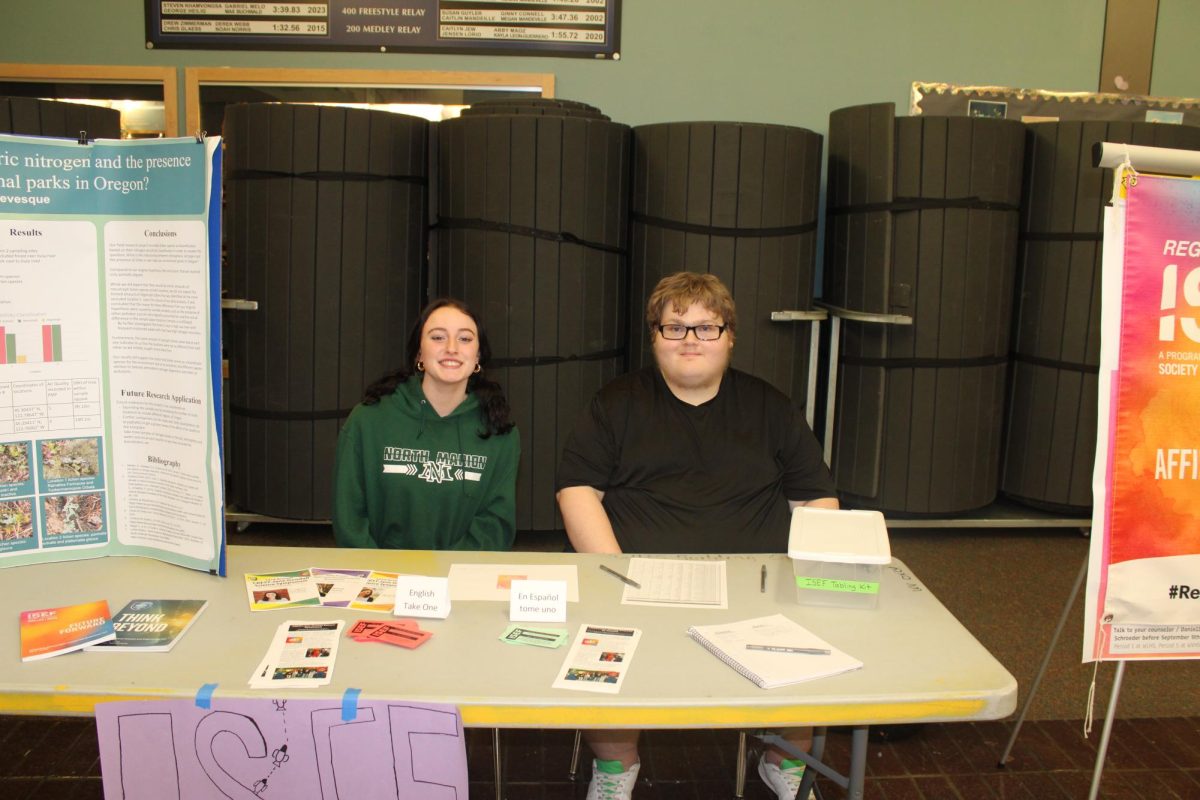 Sydney Sheldon and Cayden Whisman stop to smile for the camera. They represent the ISEF club. Sydney says, " our mission is to help guide students as they develop their Stem projects based on experiments, data research, and innovative practices and help them prosper at the fair at a competitive level."