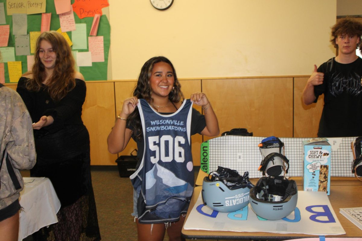 Milan De la Cruz showcases her snowboarding jersey in front of the Snowboarding club stand. She says, " our club is different than other clubs at Wilsonville because of our size. We have a lot of people that are willing to raise money. We also compete and go to state for snowboarding."