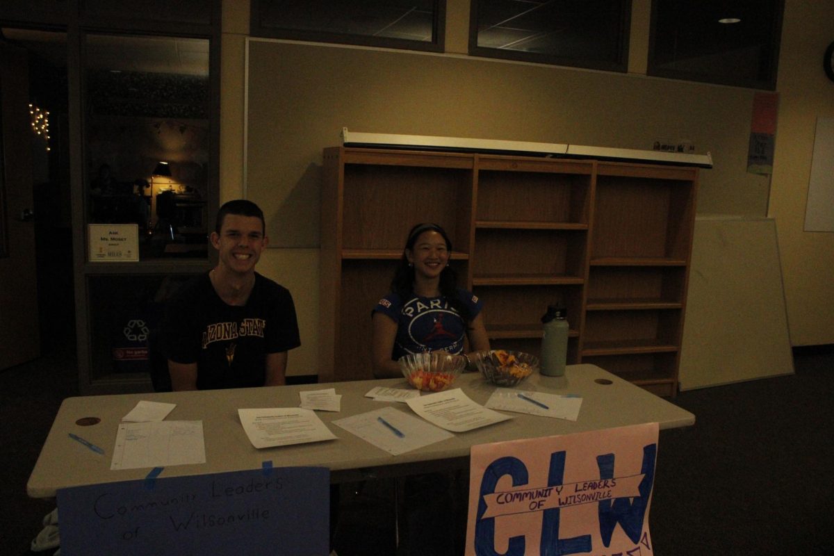 Abby Khamvongsa and Ryan Williams sit behind their club sign Community leaders of Wilsonville. Abby says, " I first joined this club because it was fun, but it now means a lot to me because it helps me feel like a better person by helping other people."