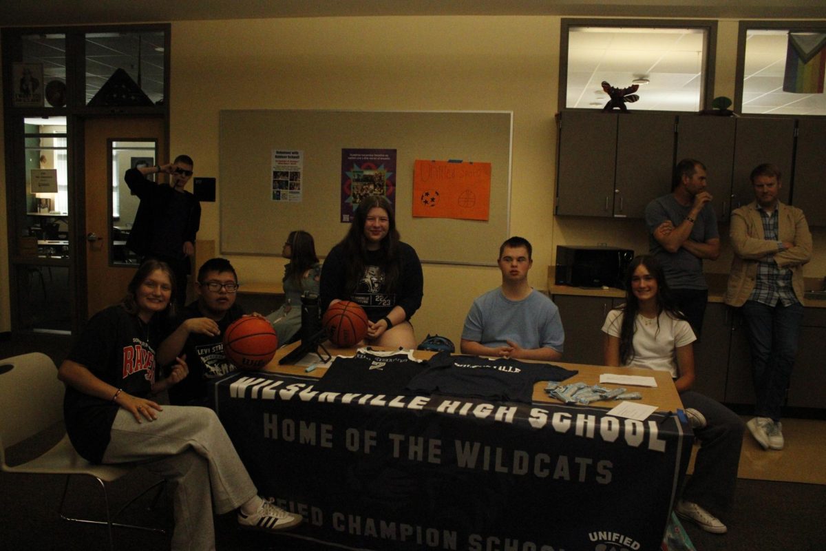 At the Unified Sports club Kylie Weisgerber sits beside her fellow club members/teammates Alex Leon-Pena, Shae Seber, and Skylar. Kylie states, " our main goal is to promote social inclusion by bringing together athletes with and without intellectual disabilities on sports teams.