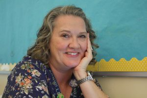 Mrs. Heaton, a tenth grade English teacher, poses in her classroom. She smiles warmly, a symbol of her joy that she carries with her teaching. 
