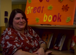 Ms. Coreson is featured in front of the new "Leaf with a great book" fall decoration, which is placed in the fiction section of Wilsonville High School's library. This decor's theme is orange, a color one would find on all of the books placed on the shelf under that poster. 