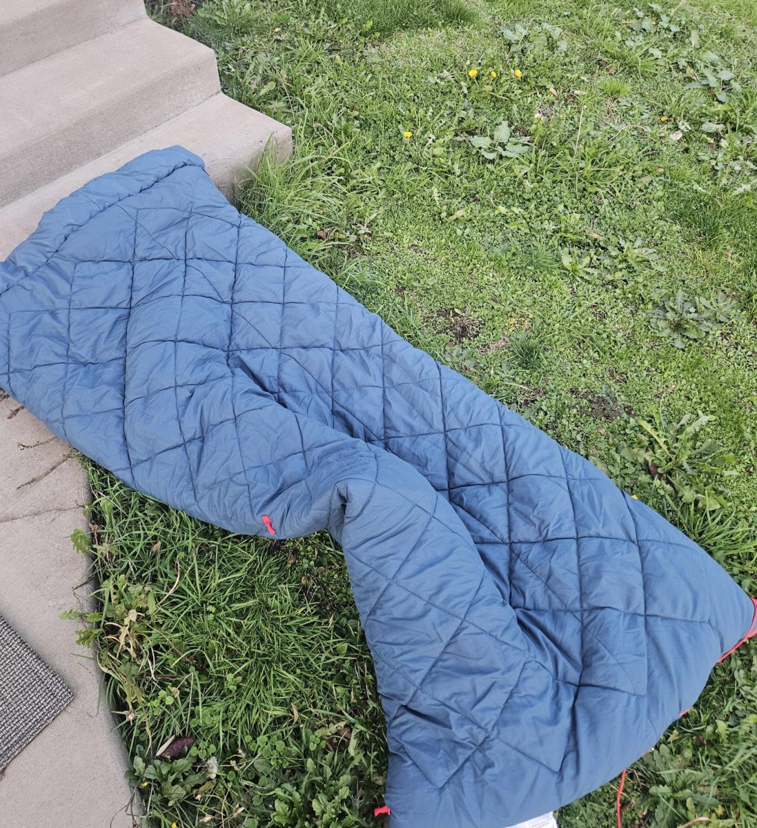 The picture features a sleeping bag laid out on the steps of concrete steps. It serves as a visual reminder of how limited options for safe rest can be for people experiencing homelessness.
