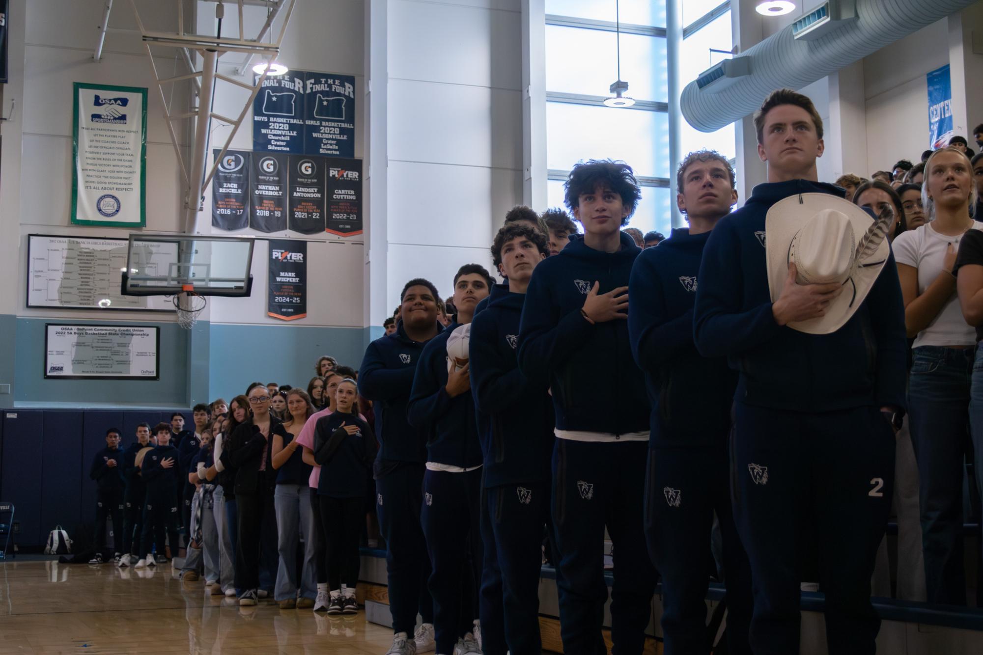 The junior section of the bleachers stands tall and proud as they set their gazes upon the flag during the playing of the national anthem. Dressed in their track suits and topped with Western hats, the boys of the front row prepare to perform a swing dance during the assembly. 