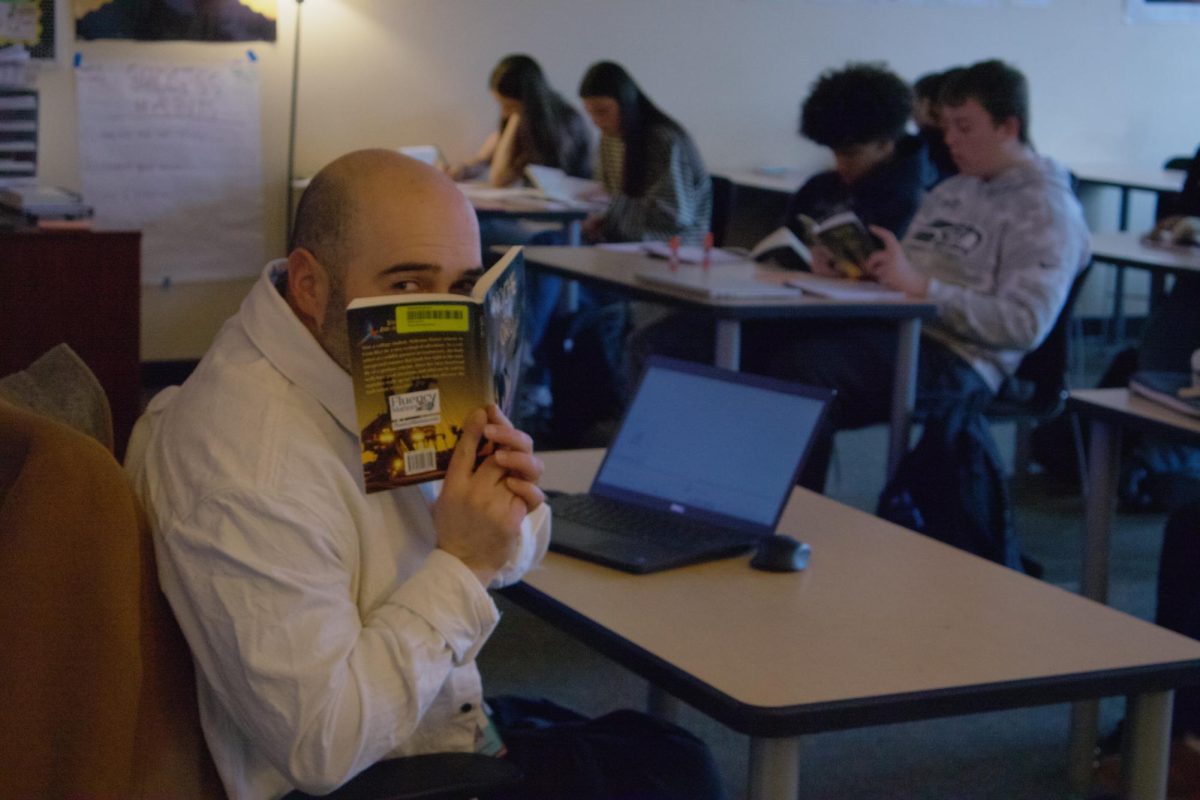 Spanish teacher Mr. Smeraglio angles himself towards the camera, holding his current book read Noche de Oro. He observes his students as they read independently or with their table partner.
