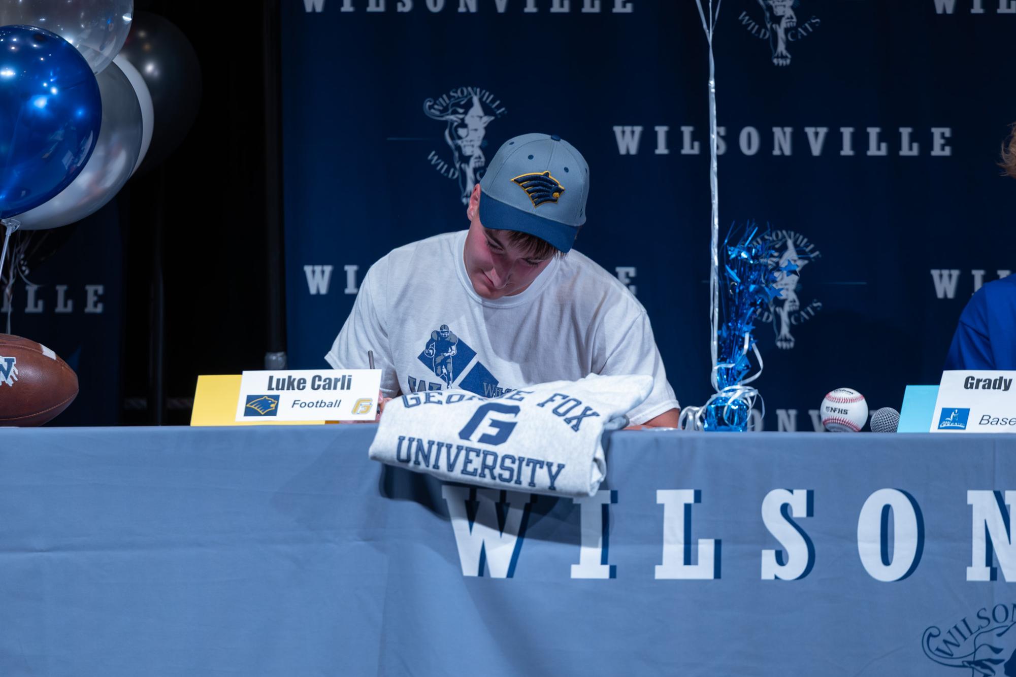 Luke Carli signs his letter of intent. He will attend George Fox University next school year.